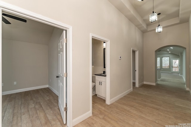 hallway with a towering ceiling, light hardwood / wood-style flooring, and a raised ceiling