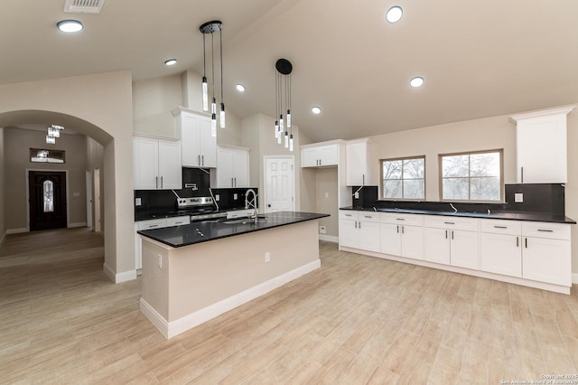 kitchen with white cabinetry, decorative light fixtures, a center island with sink, and light hardwood / wood-style flooring