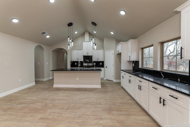 kitchen featuring tasteful backsplash, decorative light fixtures, white cabinets, and a center island with sink