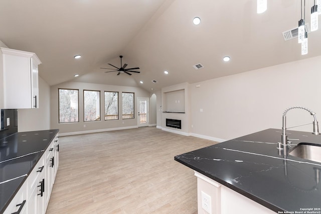 kitchen featuring lofted ceiling, sink, dark stone countertops, white cabinets, and ceiling fan