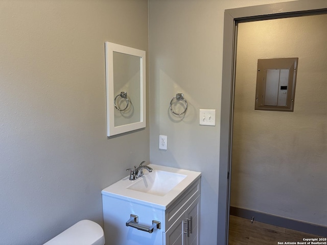 bathroom with vanity, hardwood / wood-style flooring, electric panel, and toilet