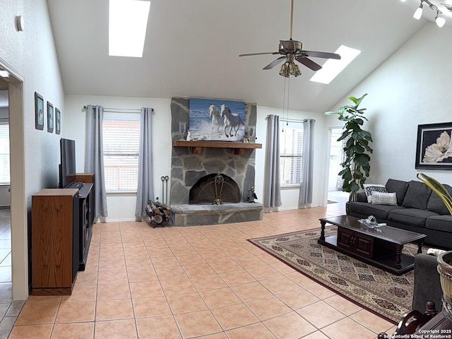 tiled living room featuring ceiling fan, a stone fireplace, a skylight, and high vaulted ceiling