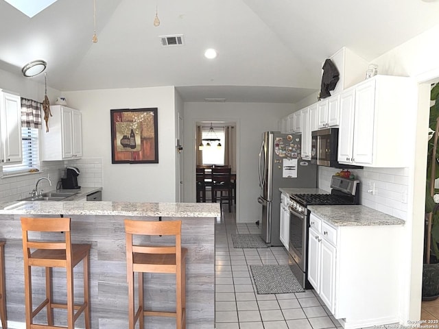 kitchen with lofted ceiling, a breakfast bar area, white cabinets, kitchen peninsula, and gas stove