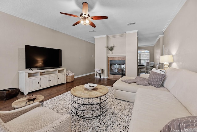 living room featuring a textured ceiling, ornamental molding, dark hardwood / wood-style flooring, a tile fireplace, and ceiling fan