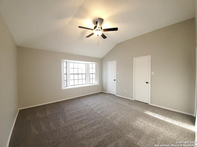 empty room featuring dark carpet, vaulted ceiling, and ceiling fan