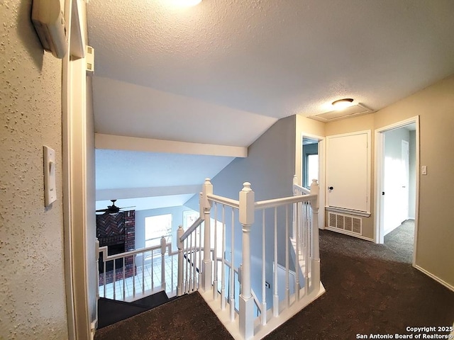 hallway with vaulted ceiling, dark carpet, and a textured ceiling