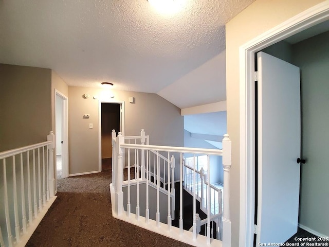 corridor with lofted ceiling, a textured ceiling, and dark colored carpet