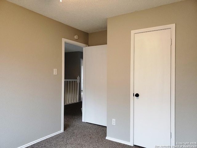 unfurnished bedroom featuring a textured ceiling and dark carpet