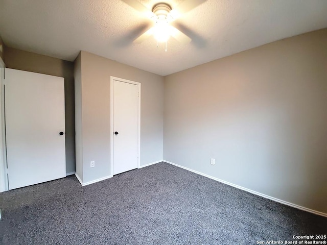 unfurnished bedroom featuring ceiling fan, dark carpet, and a textured ceiling