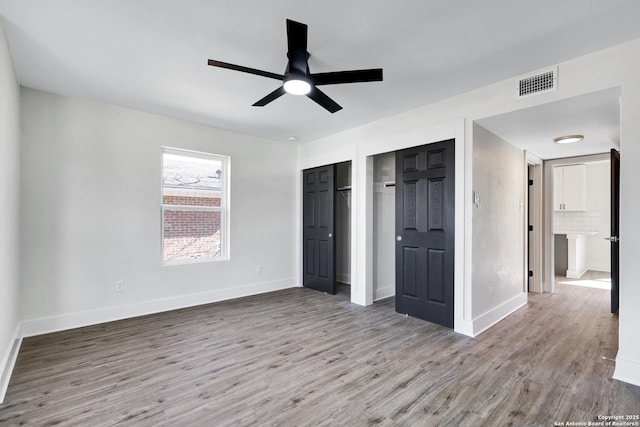 unfurnished bedroom featuring two closets, light hardwood / wood-style flooring, and ceiling fan