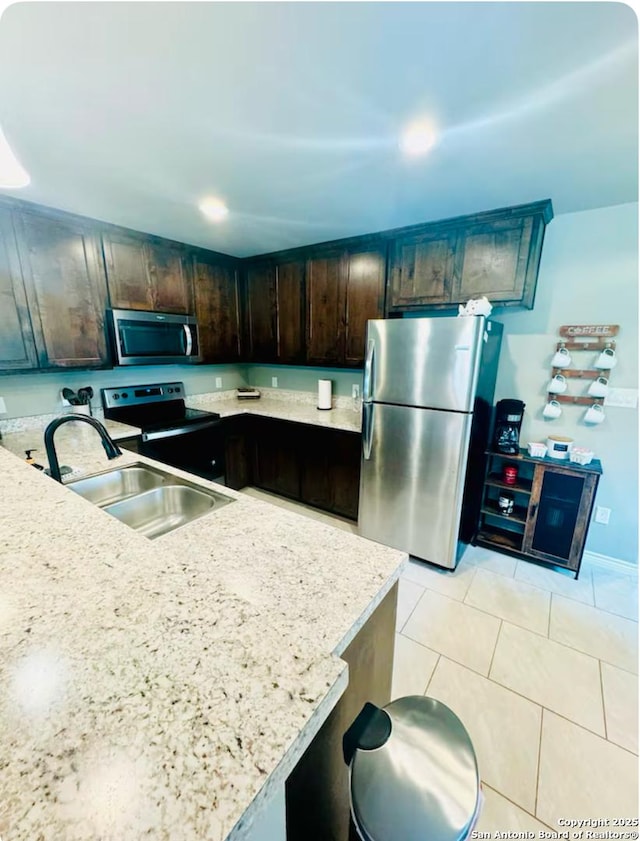 kitchen featuring sink, light stone counters, dark brown cabinets, light tile patterned floors, and stainless steel appliances