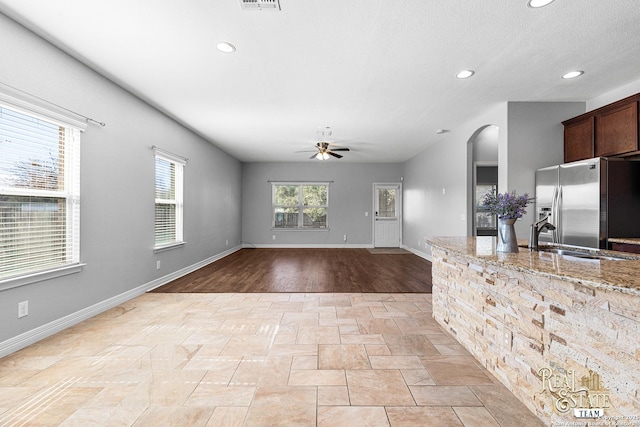 kitchen featuring sink, ceiling fan, dark brown cabinets, light stone counters, and stainless steel fridge with ice dispenser