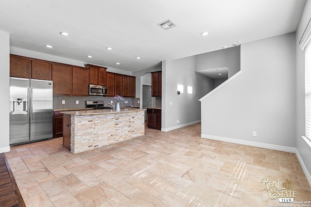 kitchen featuring stainless steel appliances, tasteful backsplash, light stone countertops, and a kitchen island with sink