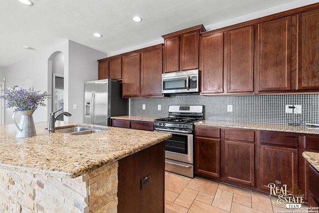 kitchen with sink, tasteful backsplash, appliances with stainless steel finishes, an island with sink, and light stone countertops