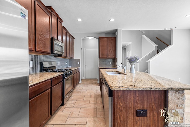 kitchen with sink, tasteful backsplash, a center island with sink, appliances with stainless steel finishes, and light stone countertops