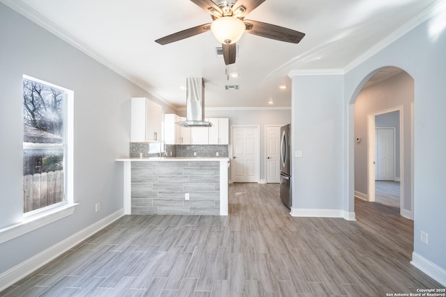 kitchen with island range hood, stainless steel refrigerator, kitchen peninsula, a healthy amount of sunlight, and white cabinets