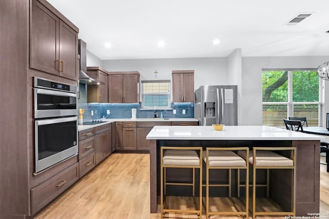 kitchen featuring stainless steel appliances, a breakfast bar, a kitchen island, and wall chimney range hood