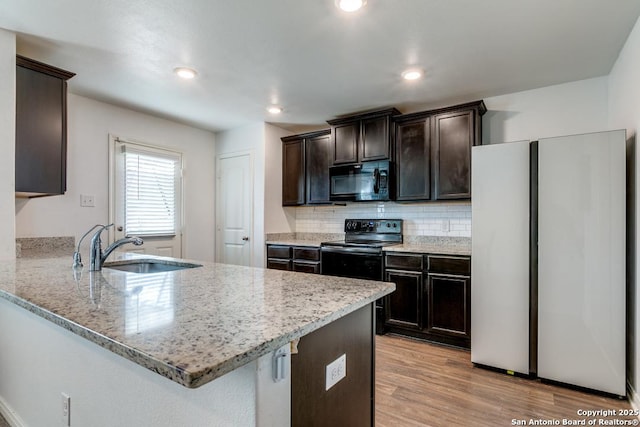 kitchen with tasteful backsplash, black appliances, sink, kitchen peninsula, and light hardwood / wood-style flooring