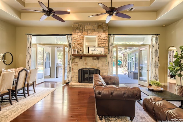 living room with a tray ceiling, dark wood-type flooring, plenty of natural light, and a stone fireplace