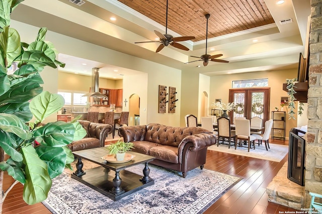 living room featuring dark wood-type flooring, ornamental molding, a stone fireplace, wooden ceiling, and a raised ceiling