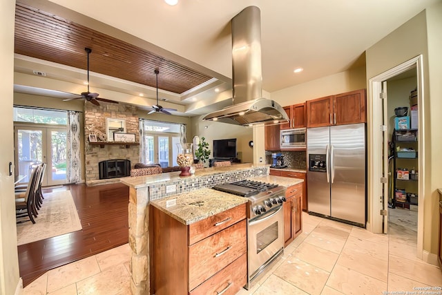 kitchen featuring island range hood, light stone counters, a tray ceiling, stainless steel appliances, and french doors