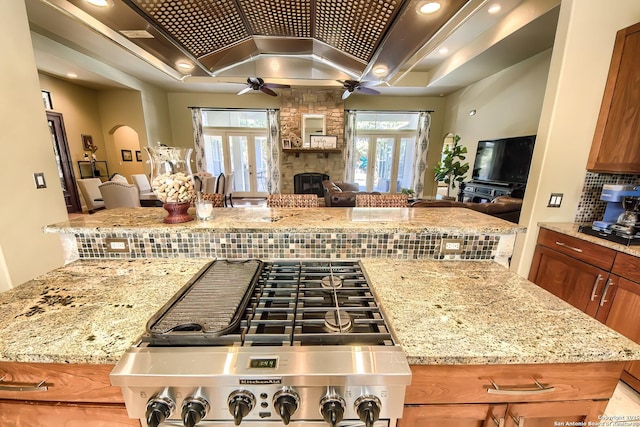 kitchen with a stone fireplace, gas stovetop, tasteful backsplash, ceiling fan, and light stone countertops