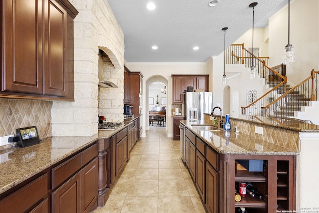 kitchen featuring sink, light stone counters, hanging light fixtures, a center island with sink, and appliances with stainless steel finishes