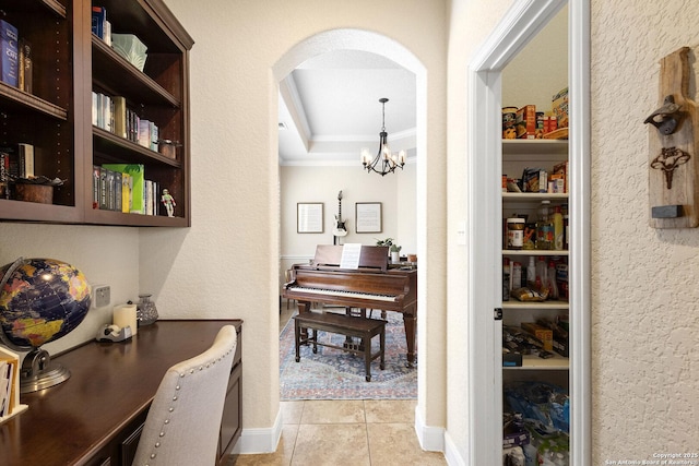 corridor featuring crown molding, a tray ceiling, an inviting chandelier, and light tile patterned floors