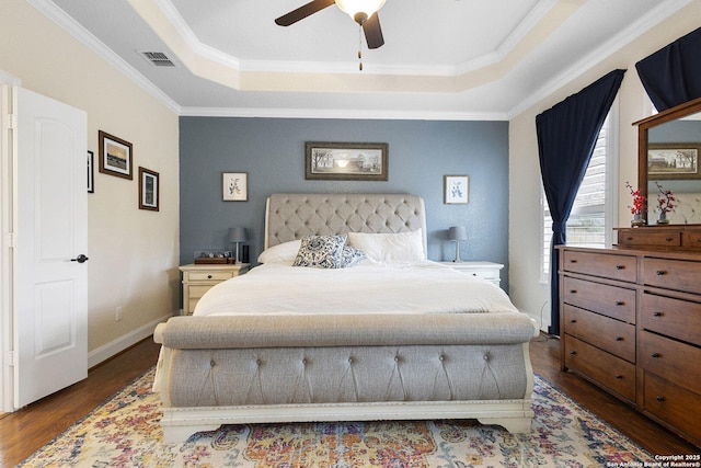 bedroom with dark wood-type flooring, ceiling fan, ornamental molding, and a tray ceiling