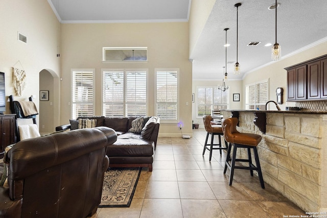 tiled living room with crown molding, a towering ceiling, and an inviting chandelier