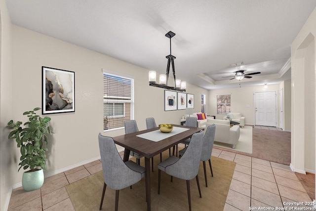 tiled dining room with ceiling fan with notable chandelier and a raised ceiling