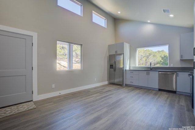 kitchen with sink, white cabinetry, light hardwood / wood-style flooring, appliances with stainless steel finishes, and a high ceiling