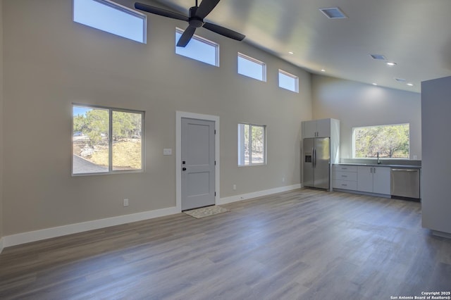 unfurnished living room featuring sink, a high ceiling, ceiling fan, and light wood-type flooring