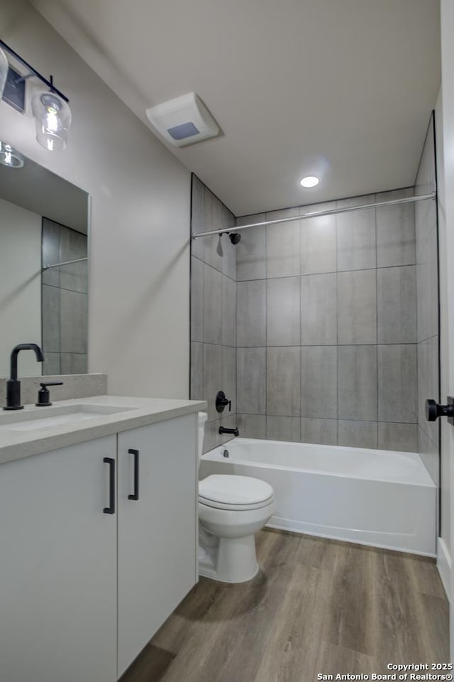 full bathroom with vanity, tiled shower / bath, hardwood / wood-style flooring, and toilet