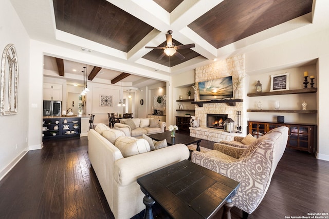 living room with coffered ceiling, a stone fireplace, dark hardwood / wood-style flooring, beamed ceiling, and ceiling fan