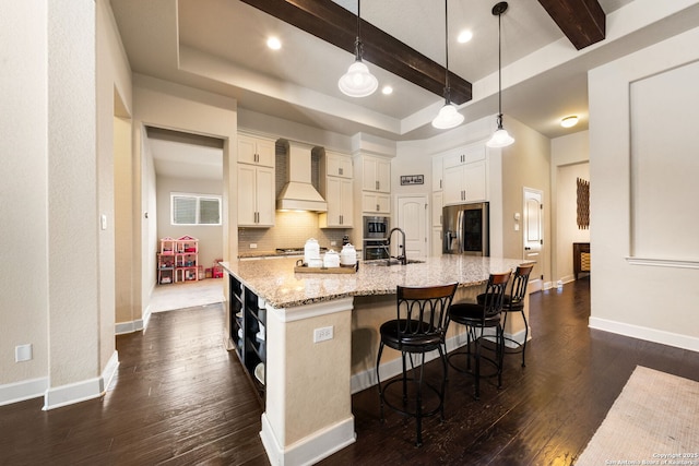 kitchen featuring appliances with stainless steel finishes, premium range hood, hanging light fixtures, light stone counters, and a large island with sink