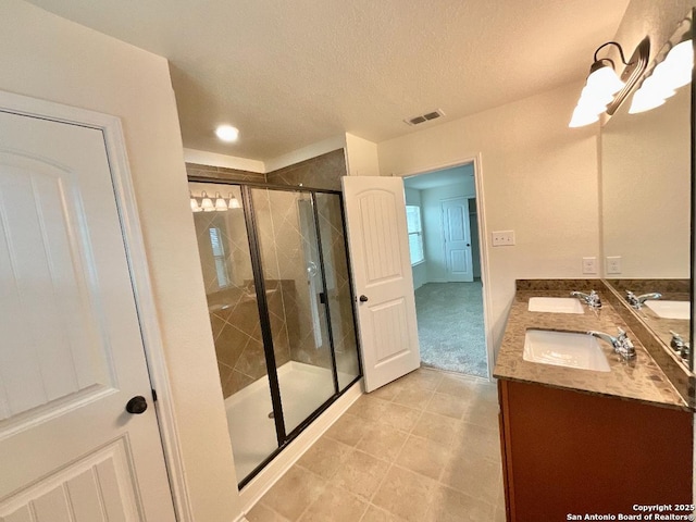 bathroom with vanity, a shower with shower door, and a textured ceiling