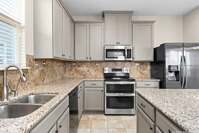 kitchen featuring sink, tasteful backsplash, light stone counters, gray cabinets, and stainless steel appliances