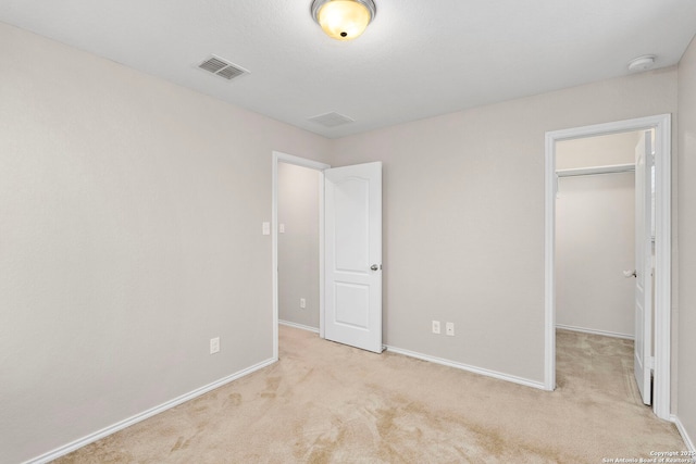 unfurnished bedroom with a walk in closet and light colored carpet