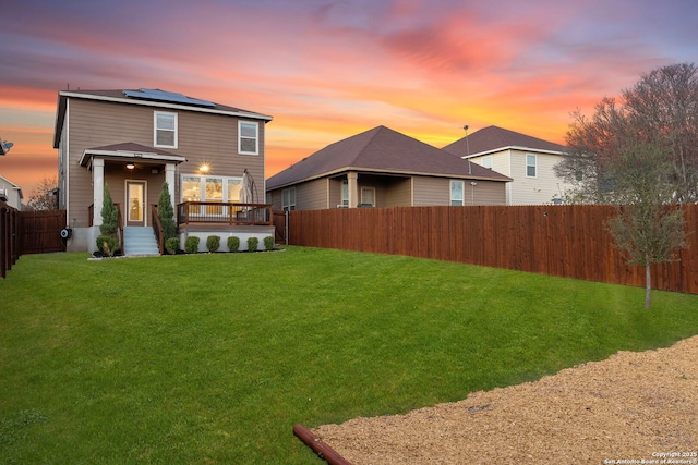 back house at dusk with a wooden deck, a yard, and solar panels