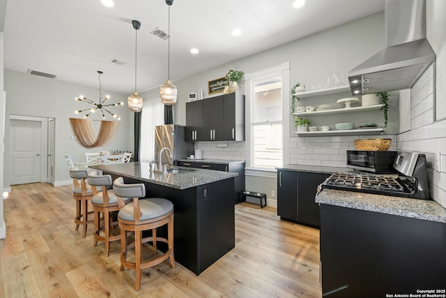 kitchen featuring a kitchen island with sink, extractor fan, light stone counters, and sink