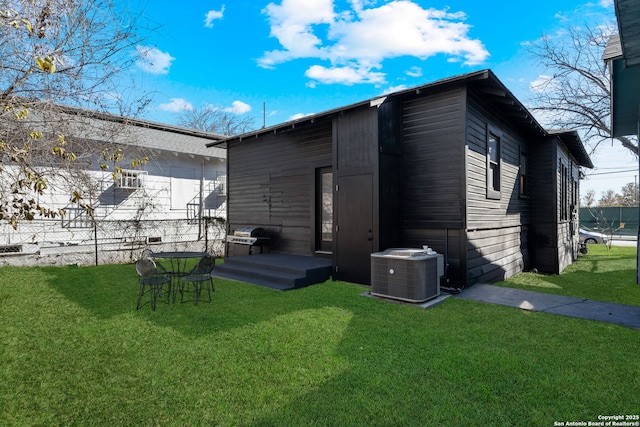 rear view of property featuring central AC unit and a lawn