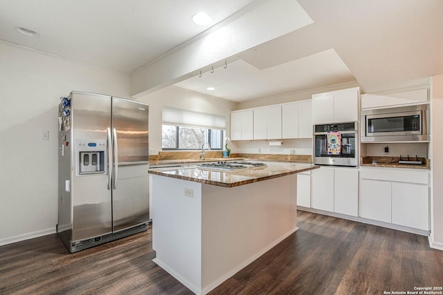 kitchen with appliances with stainless steel finishes, white cabinetry, dark stone countertops, a center island, and dark hardwood / wood-style flooring
