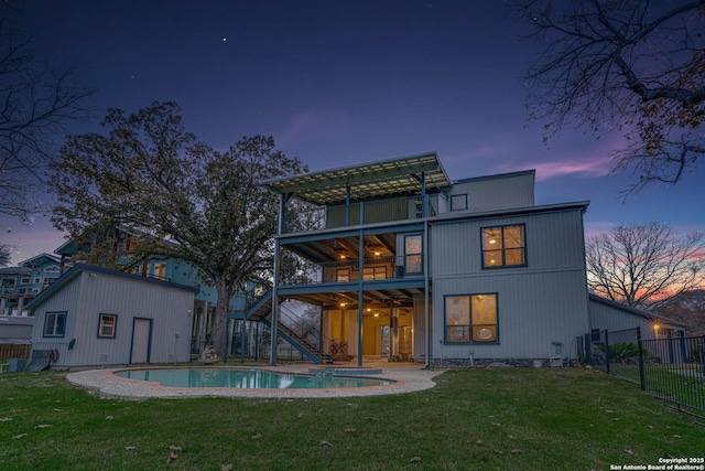 back house at dusk with a fenced in pool, a yard, and a balcony