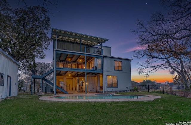 back house at dusk with a fenced in pool, a balcony, and a lawn