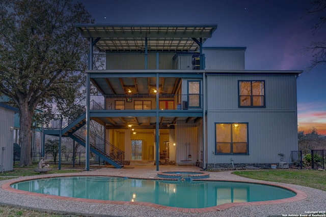 back house at dusk featuring a pool with hot tub, ceiling fan, a patio area, and a balcony