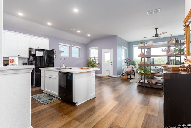 kitchen featuring sink, black appliances, hardwood / wood-style flooring, a kitchen island with sink, and white cabinets