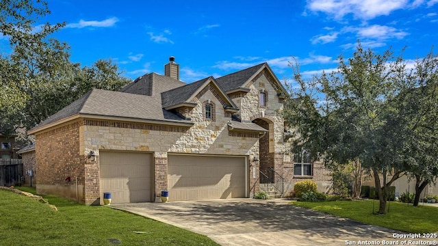 french provincial home featuring brick siding, a chimney, concrete driveway, a front yard, and a garage