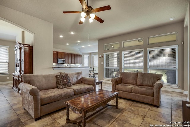 living area with arched walkways, recessed lighting, light tile patterned flooring, ceiling fan, and baseboards