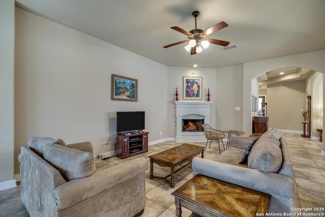 living area with baseboards, visible vents, arched walkways, a ceiling fan, and a lit fireplace